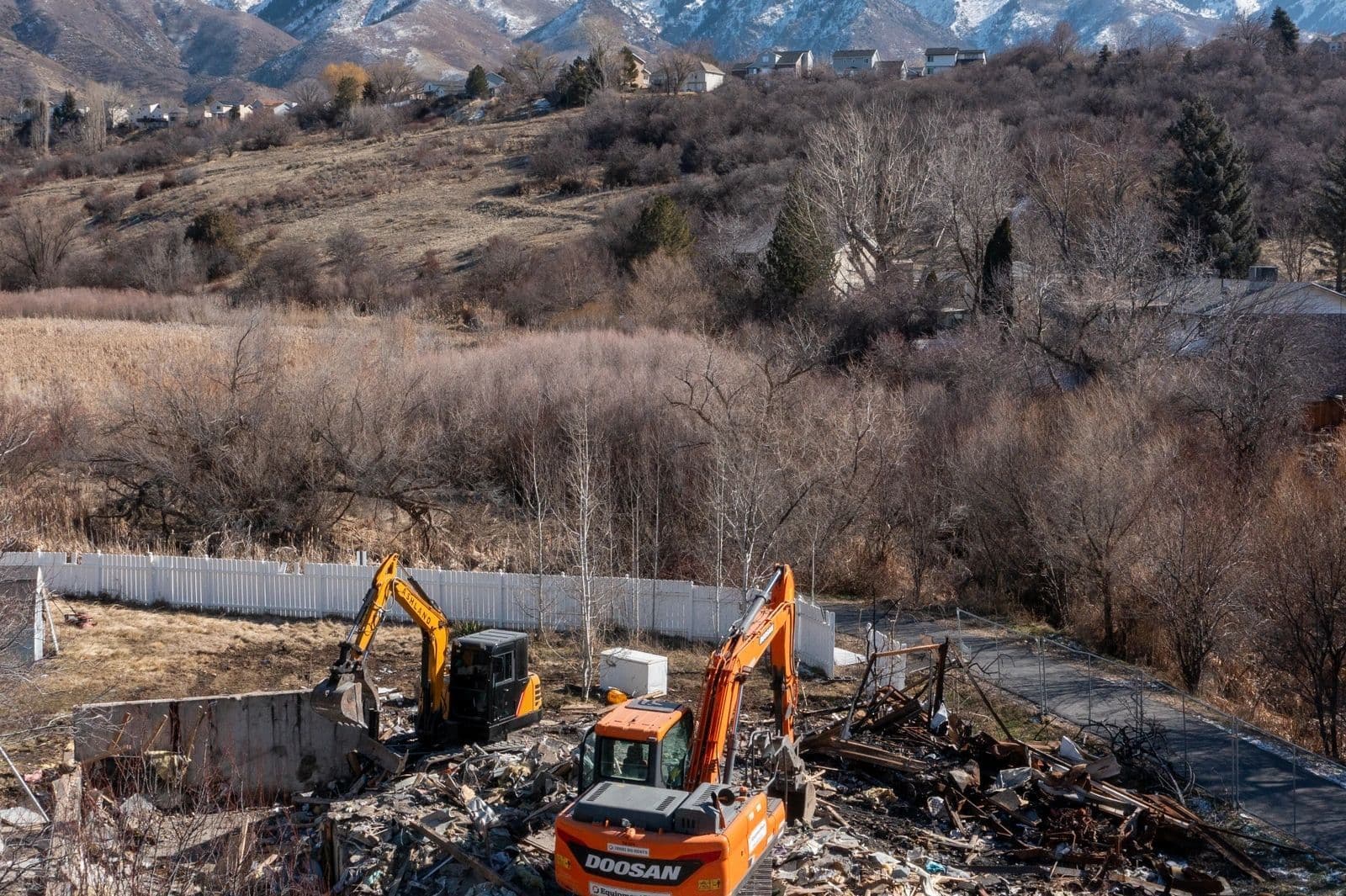 Excavators at work on a demolition site with mountains in the background and vegetation.